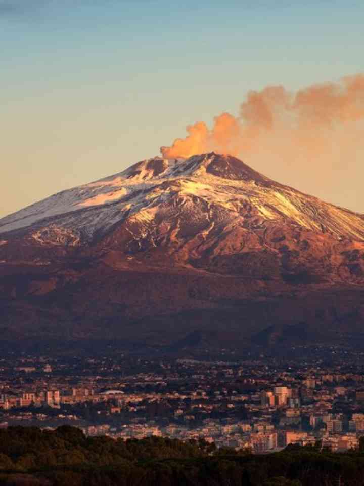 Volcano with smoke at the foot of a city